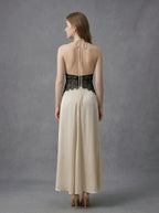 Back view of a woman in a cream satin maxi dress with black lace waist detail and a halter neckline.