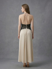 Back view of a woman in a cream satin maxi dress with black lace waist detail and a halter neckline.