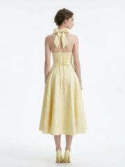 Back view of a woman in a yellow halter neck midi dress with corset detailing and a bow at the neck.
