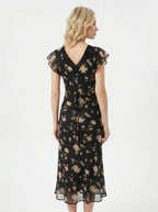 Back view of a woman in a black floral print midi dress with a tie waist.