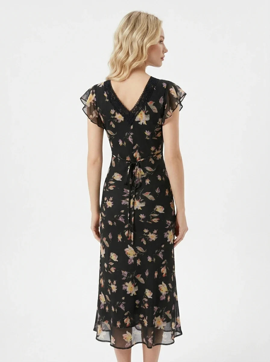 Back view of a woman in a black floral print midi dress with a tie waist.