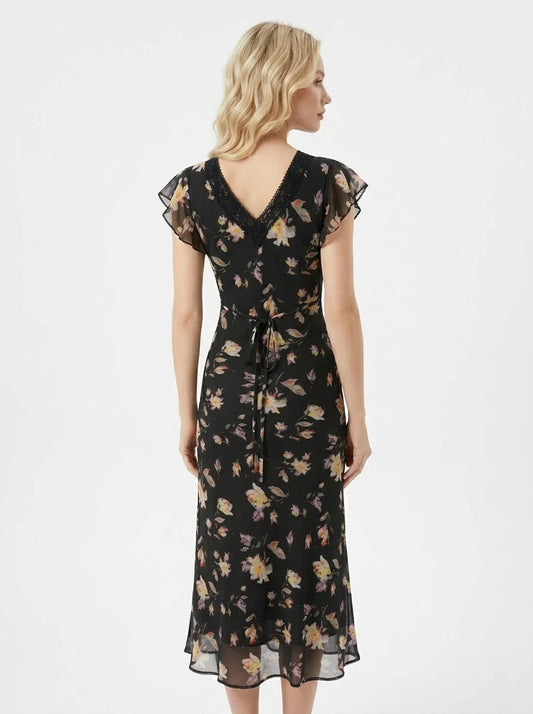Back view of a woman in a black floral print midi dress with a tie waist.