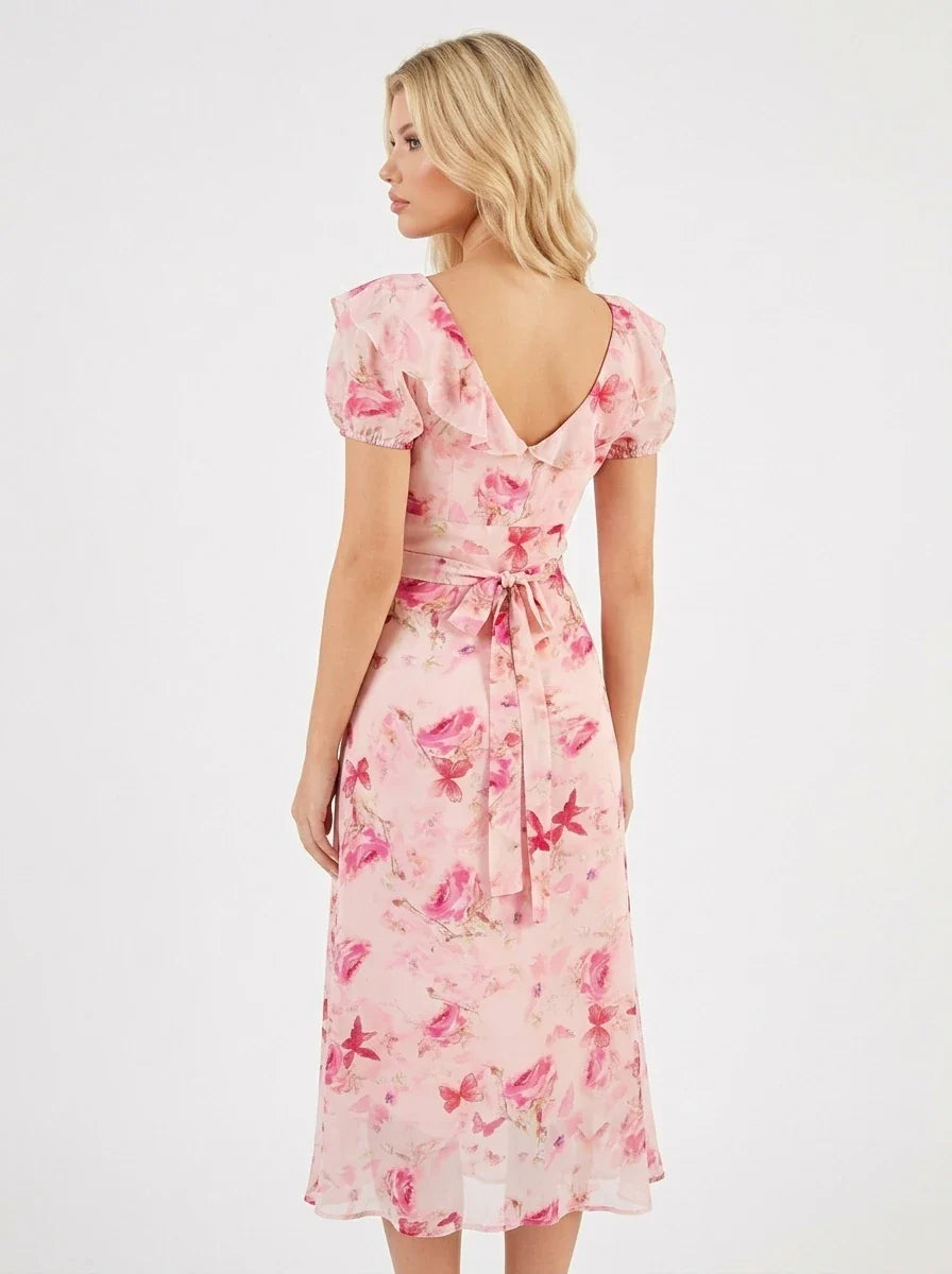 Woman wearing a pink floral print midi dress with short puff sleeves and a tie-front V-neckline, shown from the back.