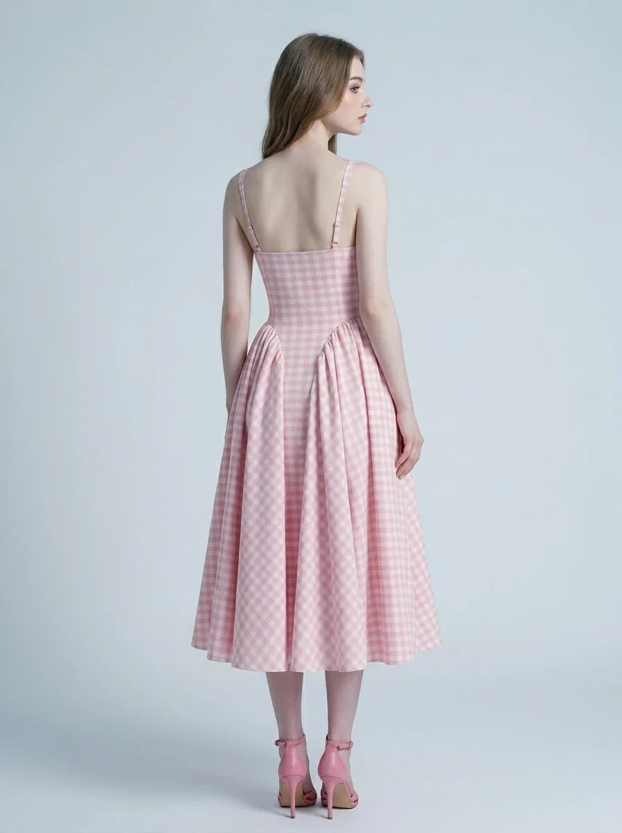 A woman models the back of a pink and white gingham midi dress with a square neckline and a full, pleated skirt, standing against a plain background.