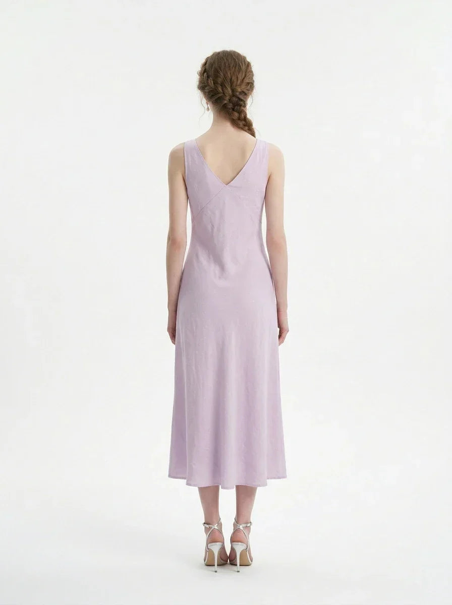 Back view of a model wearing a lavender midi dress with a V-neckline and sleeveless design, standing against a white background.