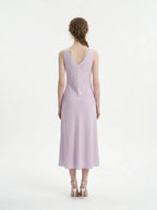 Back view of a model wearing a lavender midi dress with a V-neckline and sleeveless design, standing against a white background.