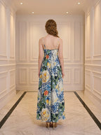 Back view of a woman in a long, sleeveless maxi dress with a colorful fruit and floral print, standing in a hallway.