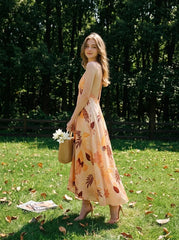 Woman standing in a grassy area with trees in the background, wearing a long, floral print, halter neck dress with an open back, carrying a straw basket.