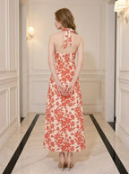 Back view of a woman wearing a cream and coral floral print halter midi dress.