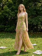 woman in a green floral strapless maxi dress with a high slit standing on a lawn with scattered papers