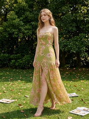 woman in a green floral strapless maxi dress with a high slit standing on a lawn with scattered papers