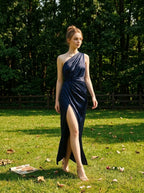 Woman in a navy blue satin one-shoulder gown with a high slit walking in a grassy park