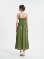 Back view of a woman in a green linen midi dress with a smocked bodice and square neckline.