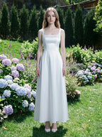 Woman wearing a white satin sleeveless A-line wedding dress with a square neckline, standing in a garden with hydrangeas