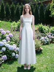 Woman wearing a white satin sleeveless A-line wedding dress with a square neckline, standing in a garden with hydrangeas