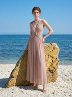 Woman in a rose gold shimmering metallic A-line V-neck sleeveless floor-length formal gown, standing on a beach