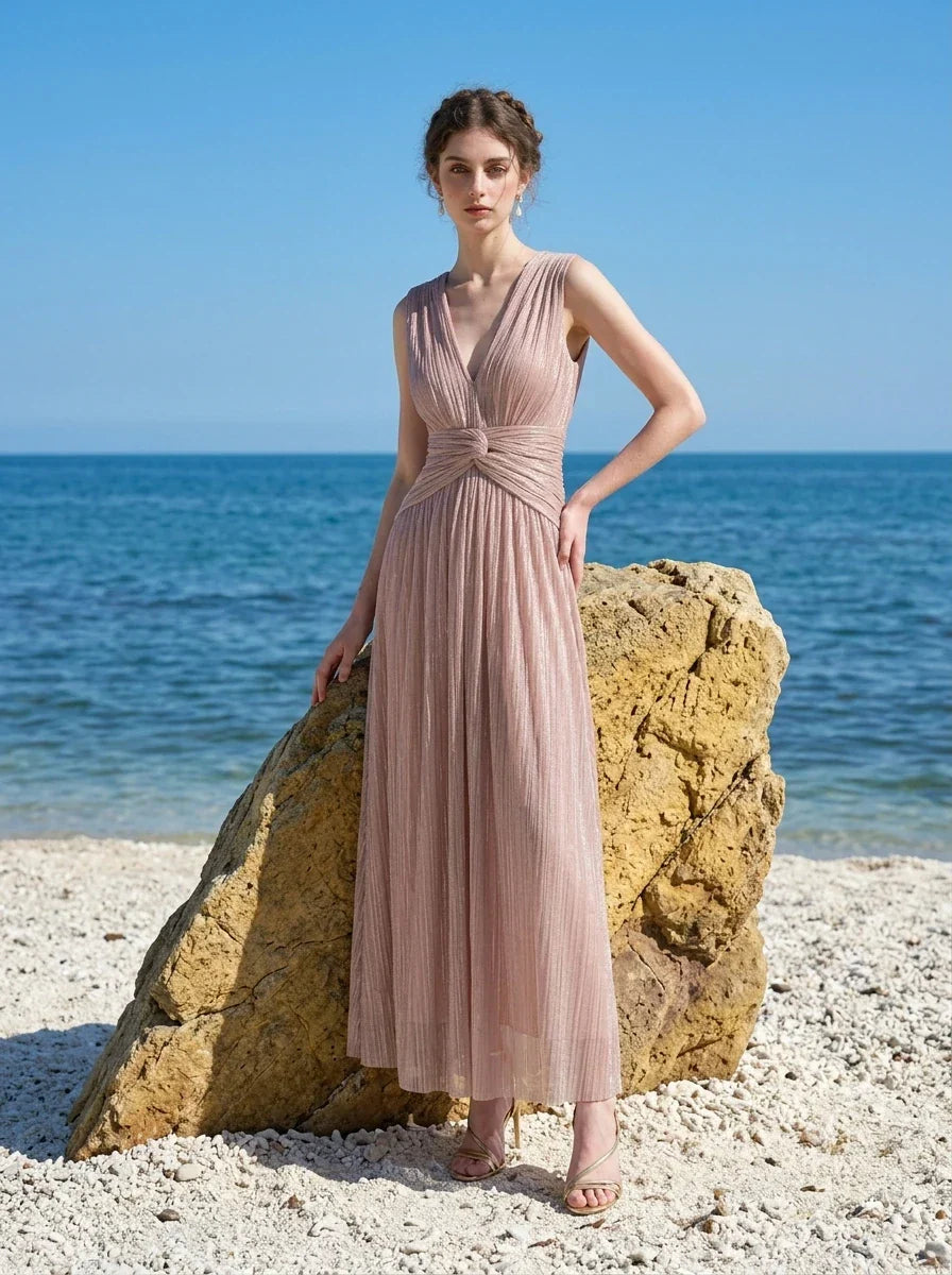 Woman in a rose gold shimmering metallic A-line V-neck sleeveless floor-length formal gown, standing on a beach