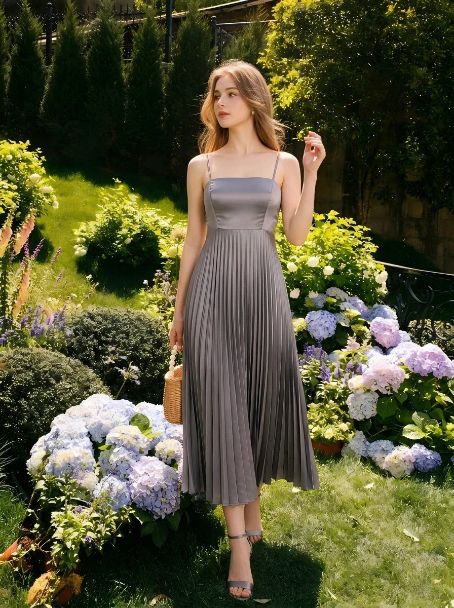 Woman wearing a grey satin midi dress with spaghetti straps and a square neckline, standing in a garden with hydrangeas.