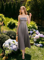 Woman wearing a grey satin midi dress with spaghetti straps and a square neckline, standing in a garden with hydrangeas.