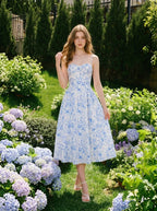 Woman wearing a blue and white floral print midi dress with spaghetti straps, standing in a garden with hydrangeas.