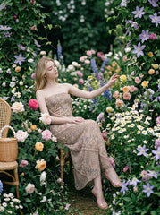 Woman wearing a strapless, patterned maxi dress sitting in a garden surrounded by flowers.
