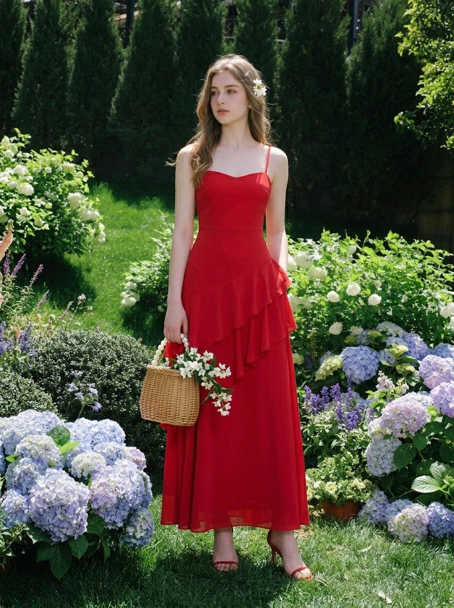 Woman wearing a red floor-length chiffon dress with tiered ruffles and spaghetti straps, holding a wicker basket with flowers in a garden setting.