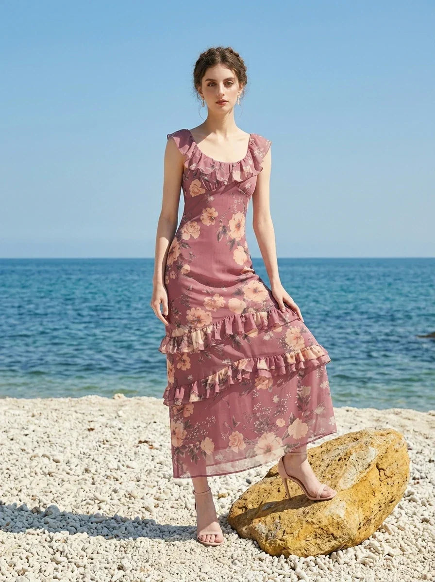 Woman wearing a pink floral print maxi dress on a beach with rocks and the ocean