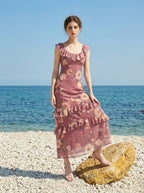 Woman wearing a pink floral print maxi dress on a beach with rocks and the ocean