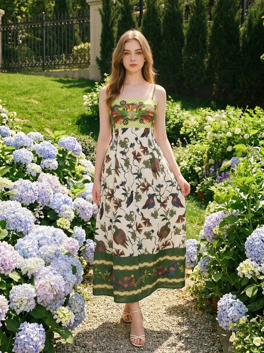 Woman walking in a garden wearing a floral and bird print midi dress with spaghetti straps and a square neckline.