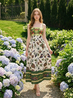Woman walking in a garden wearing a floral and bird print midi dress with spaghetti straps and a square neckline.
