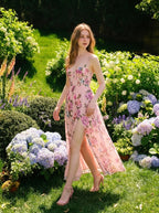 Woman wearing a pink floral print maxi dress with spaghetti straps and a high slit, walking through a lush garden.