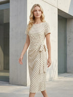 Woman wearing a cream and black polka dot midi wrap dress with short sleeves, walking outdoors against a modern building facade.