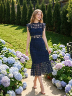Woman in a navy blue lace mermaid dress with a high neck and cap sleeves, walking through a garden with hydrangeas.