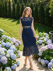 Woman in a navy blue lace mermaid dress with a high neck and cap sleeves, walking through a garden with hydrangeas.