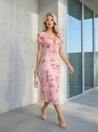 Woman walking outdoors in a pink floral print midi dress, carrying a clutch.