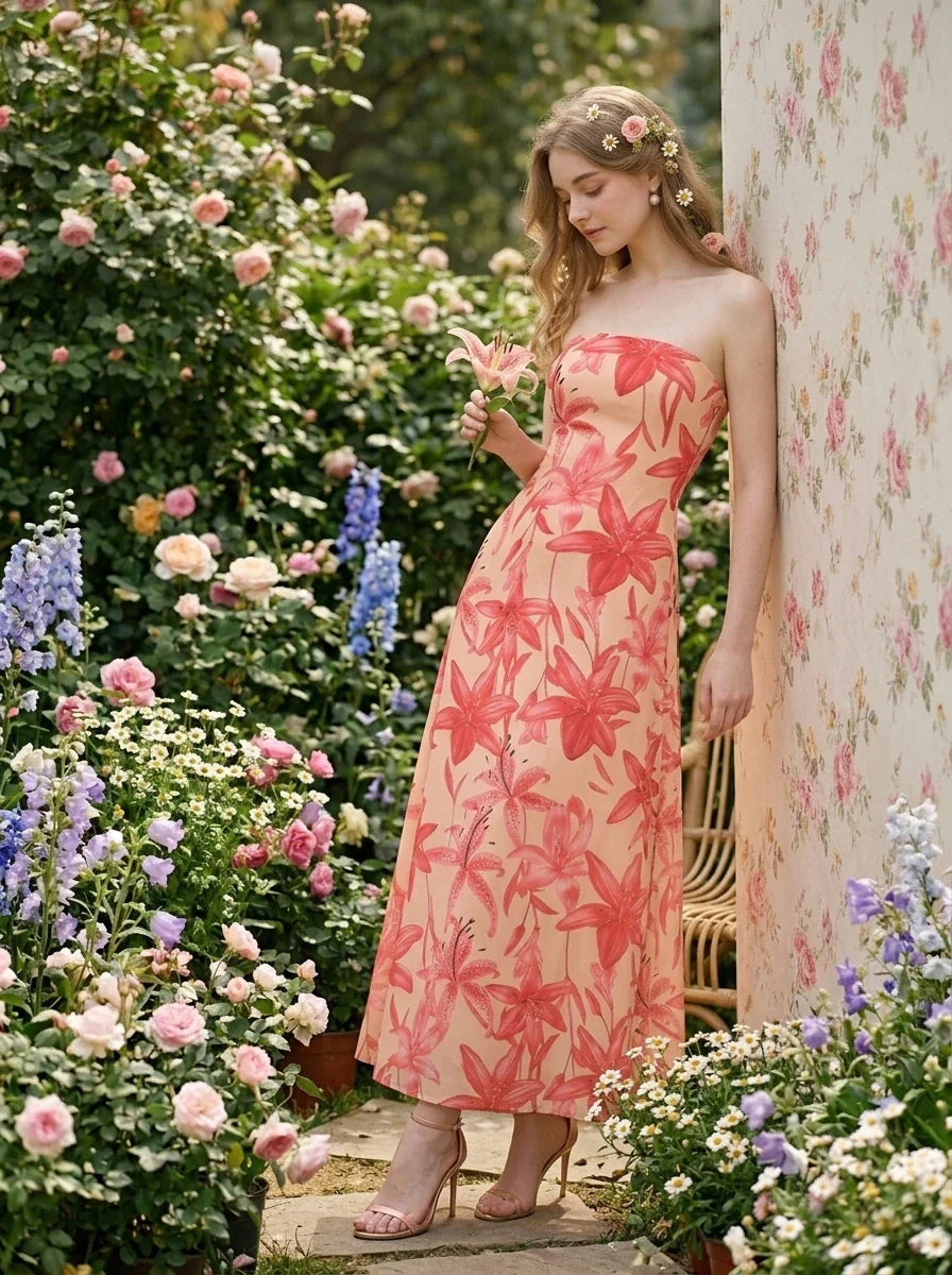 Woman leaning against a wall in a garden, holding a flower, wearing a strapless floral print midi dress.