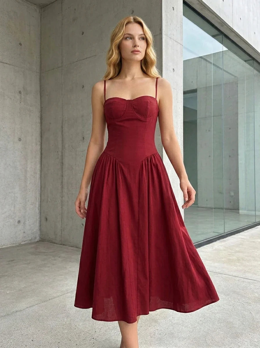 Woman wearing a deep red fit and flare midi dress with spaghetti straps, standing outdoors in a modern architectural setting