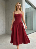 Woman wearing a deep red fit and flare midi dress with spaghetti straps, standing outdoors in a modern architectural setting