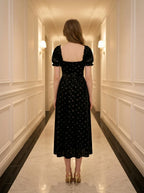 The back of a woman wearing a black velvet midi dress with a floral print.