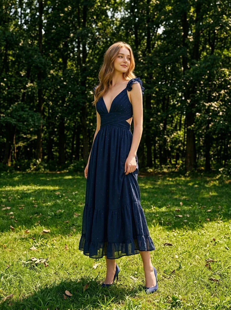 Woman standing in a park wearing a navy blue midi dress with ruffle sleeves and a deep V-neckline.