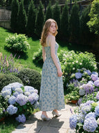 Woman in a floral print midi dress with hydrangea bushes in the background.