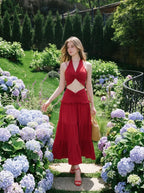 Woman wearing a red halter crop top and a tiered maxi skirt, walking through a garden path
