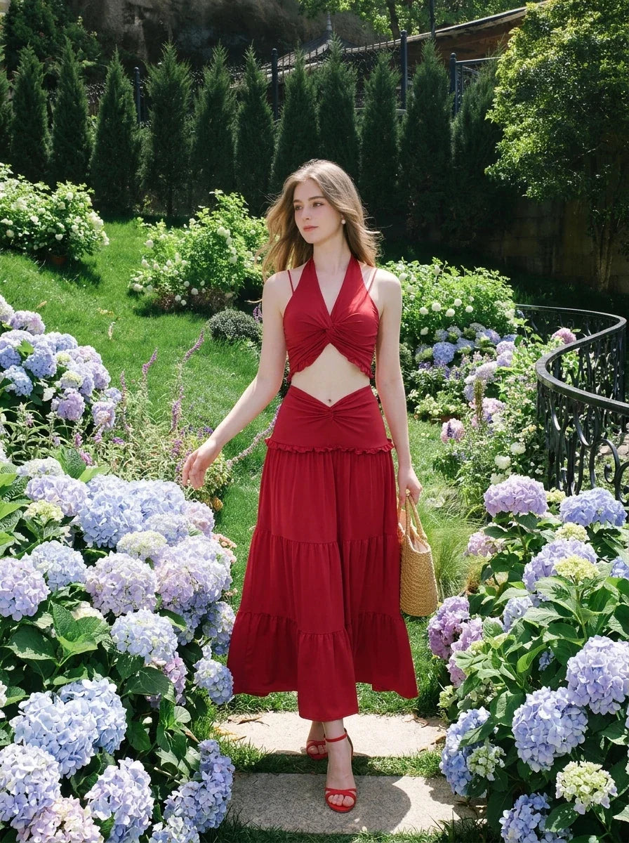 Woman wearing a red halter crop top and a tiered maxi skirt, walking through a garden path