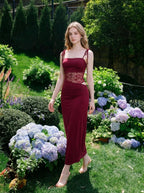 Woman walking in a garden wearing a burgundy slip dress with lace waist detailing and hydrangeas in the background.