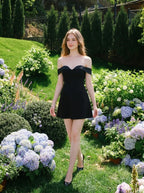 Woman walking in a garden wearing a black off-the-shoulder dress