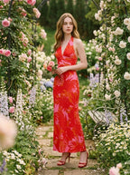 Woman in a red and pink tropical print halter maxi dress holding a bouquet of flowers in a garden