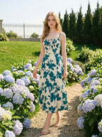 Woman wearing a floral print midi dress with spaghetti straps and a tie front detail, walking in a garden with hydrangeas.