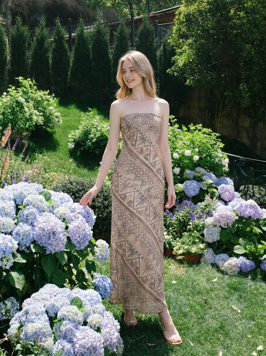 Woman wearing a strapless, patterned maxi dress posing in a garden with hydrangeas.