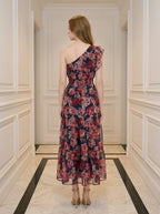 Back view of a woman wearing a navy floral print one-shoulder dress with a tiered skirt and ruffle detail, standing in a hallway.