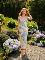 Woman wearing a cream and blue floral print satin midi dress, posing in a garden with hydrangeas.